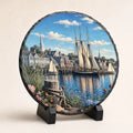 Temporary visual preview of a six-inch round photo slate with a coastal harbor design, displayed on a black stand.